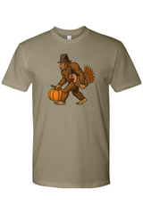 Light olive green Thanksgiving t-shirt with bigfoot sasquatch holding a pumpkin and a turkey design funny humor fall holiday short sleeve shirt